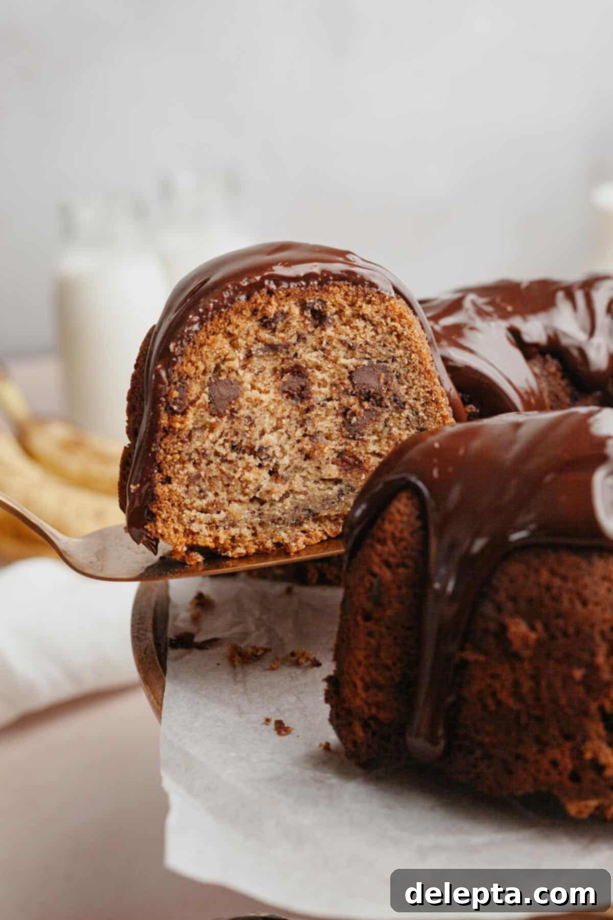 Decadent Chocolate Chip Banana Bundt Cake 2 A perfectly baked, golden-brown chocolate chip banana bundt cake slice being lifted from the cake with a silver server, revealing its moist interior and melted chocolate chips.