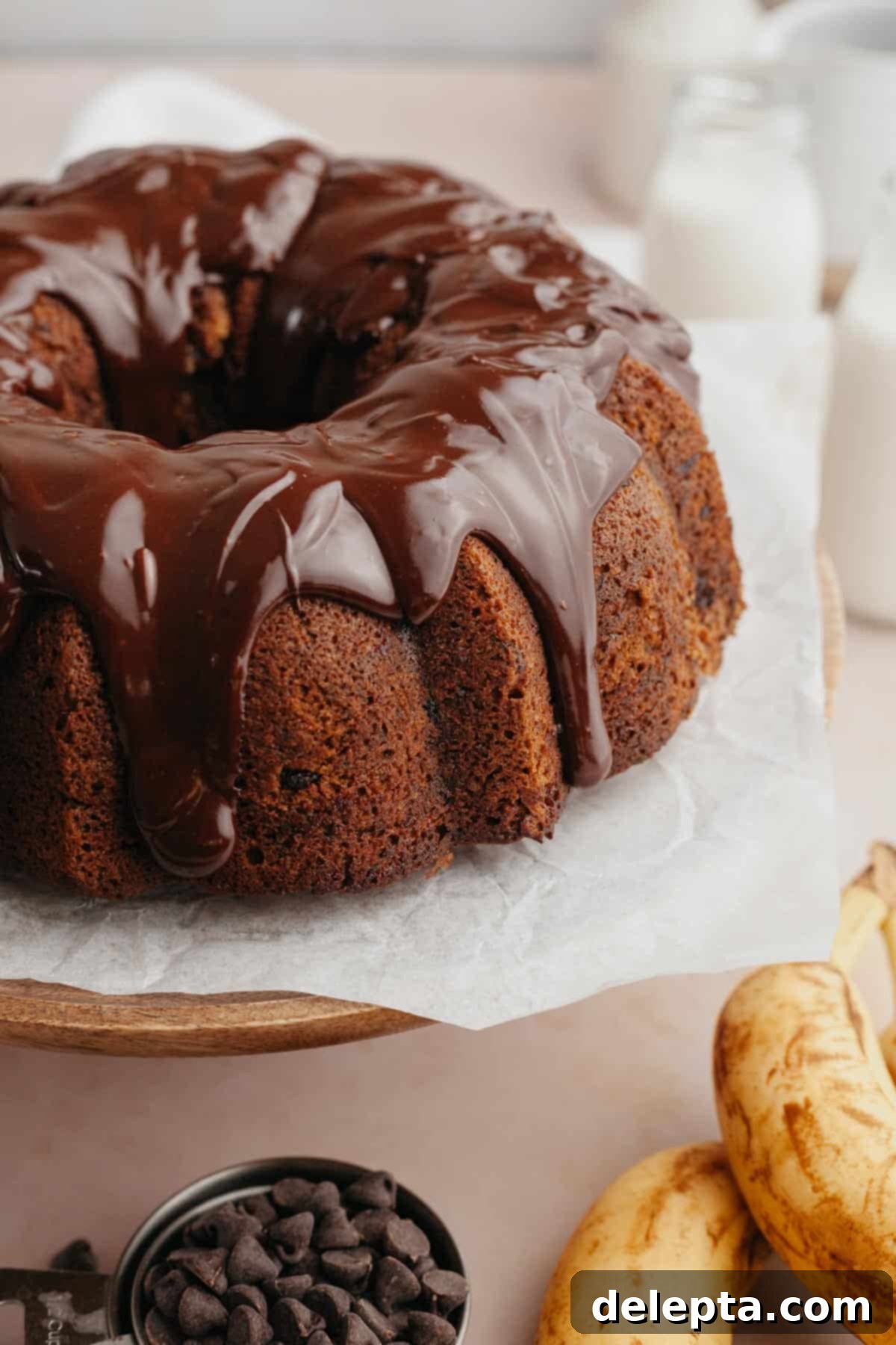 Decadent Chocolate Chip Banana Bundt Cake 8 A beautifully glazed chocolate chip banana bundt cake sitting on an elegant white cake stand, adorned with a luscious chocolate ganache.