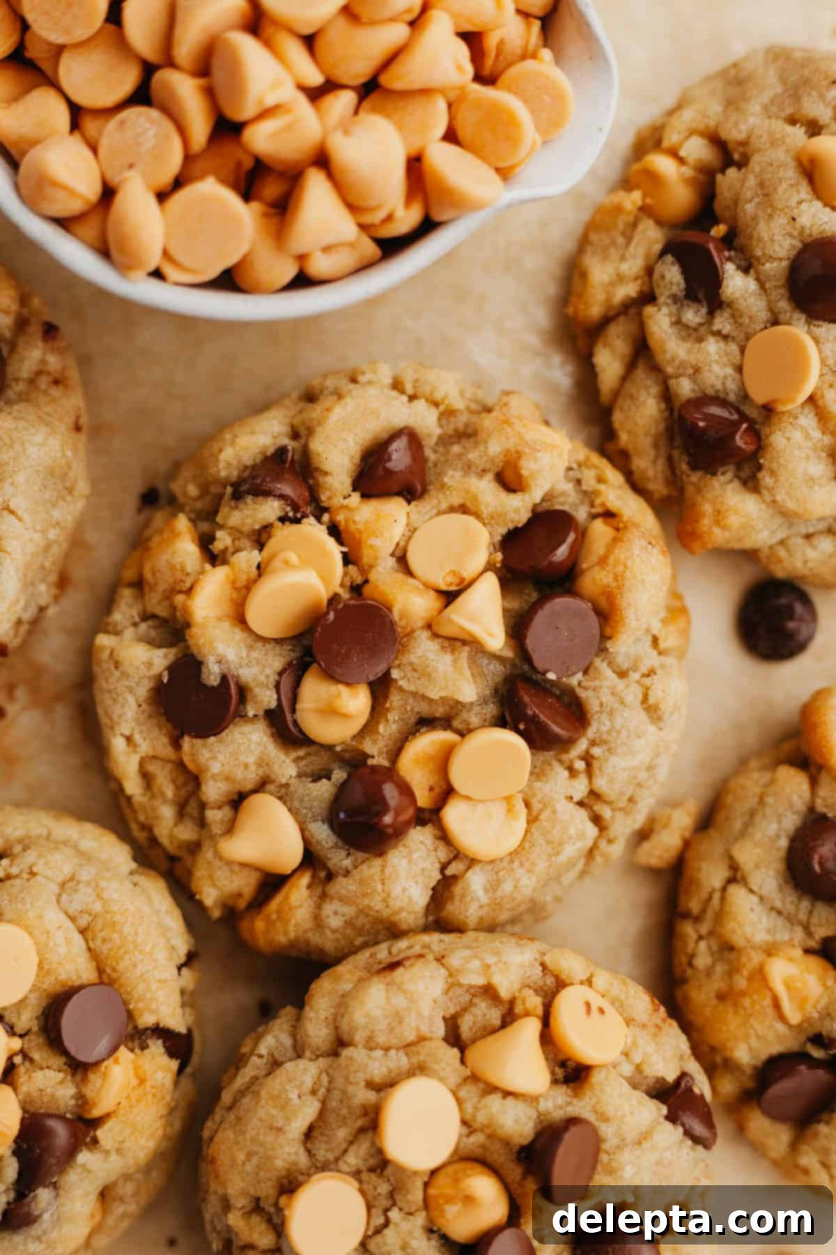 Golden Butterscotch Chocolate Chip Delights 2 Freshly baked butterscotch chocolate chip cookies cooling on light brown parchment paper, showcasing their soft texture and abundant chips.
