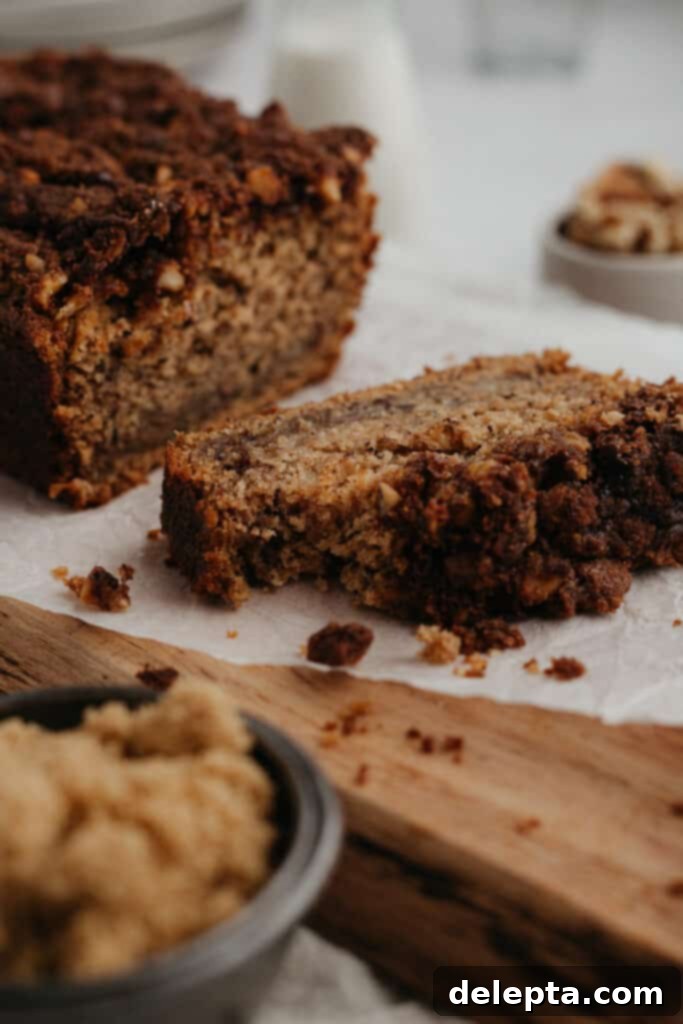 Cinnamon Crumble Banana Bread 15 Freshly baked cinnamon crunch banana bread on a wooden board with a slice cut, showing its moist interior and crispy topping