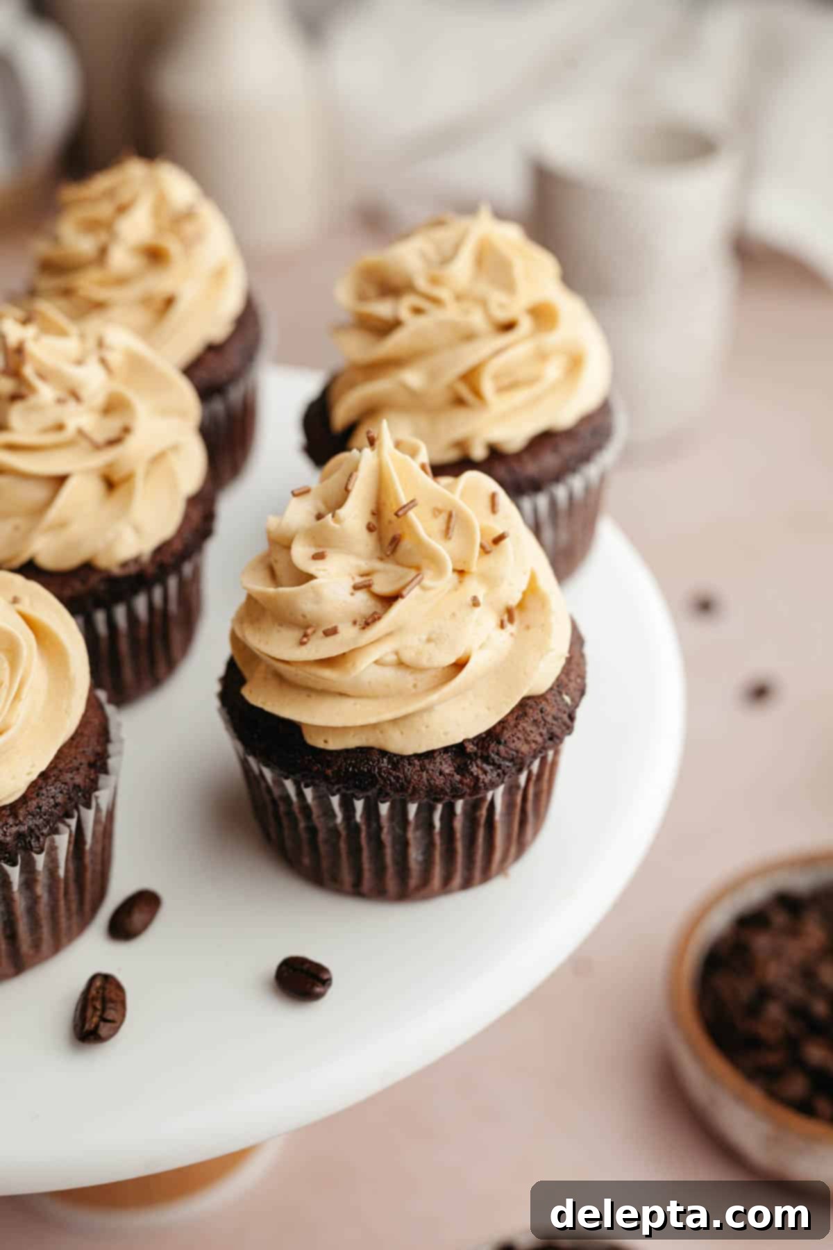 Effortlessly Moist Mocha Cupcakes with Espresso Buttercream 2 Chocolate cupcakes with coffee frosting on a white cake stand.