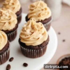 Effortlessly Moist Mocha Cupcakes with Espresso Buttercream 12 Chocolate cupcakes with coffee frosting on a white cake stand.