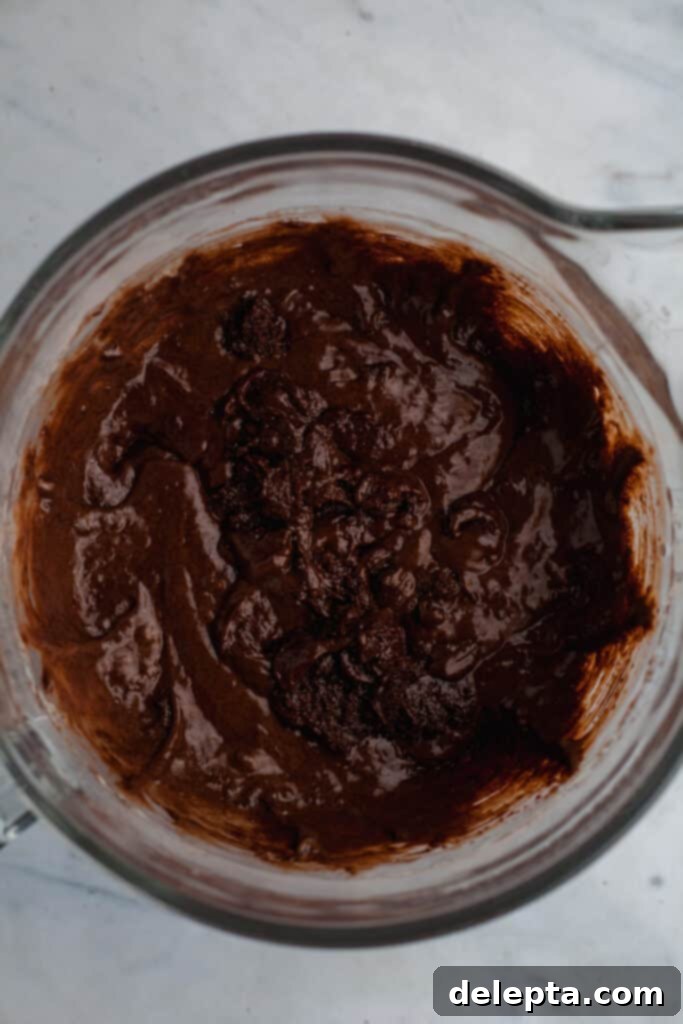Decadent Oreo Drip Cake 6 Chocolate cake batter being mixed in a glass bowl, showcasing its smooth texture
