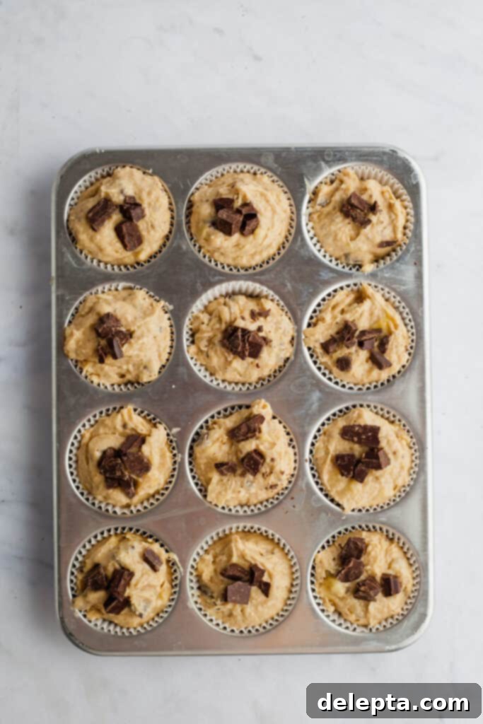 Irresistible Chocolate Chip Peanut Butter Muffins 9 A muffin tray lined with paper cases, filled to the brim with unbaked peanut butter banana muffin batter, topped with extra chocolate chunks.