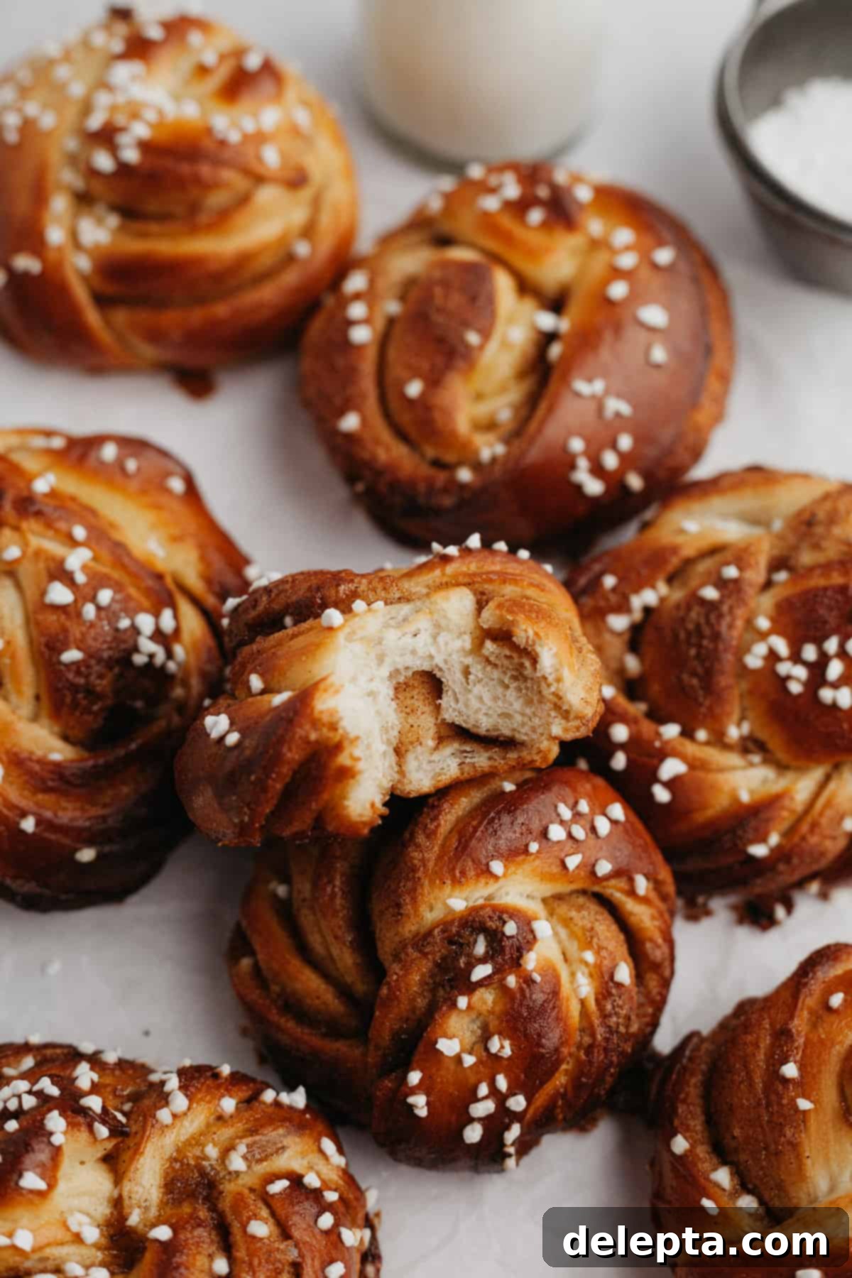 Pillowy Swedish Cinnamon Swirls 2 Several soft and fluffy Swedish cinnamon buns on a marble surface, one has a bite taken out of it revealing the delicious cardamom and cinnamon filling. They are perfectly golden brown and sprinkled with pearl sugar.