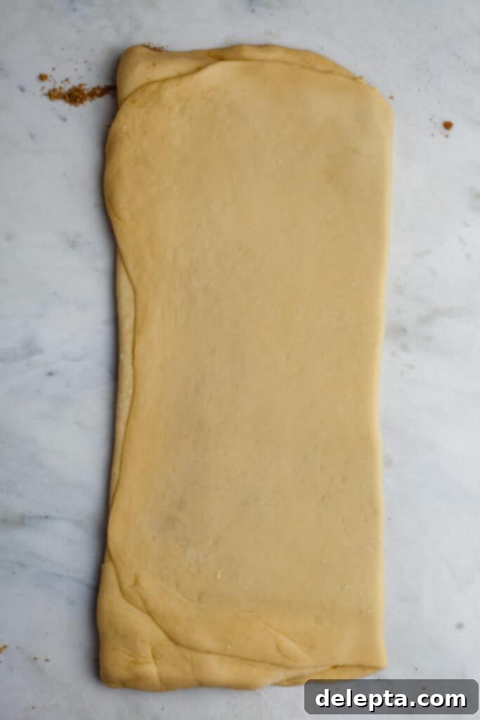 Pillowy Swedish Cinnamon Swirls 14 A long, rectangular piece of folded dough on a marble counter, indicating the second fold has been completed, resulting in three layers.
