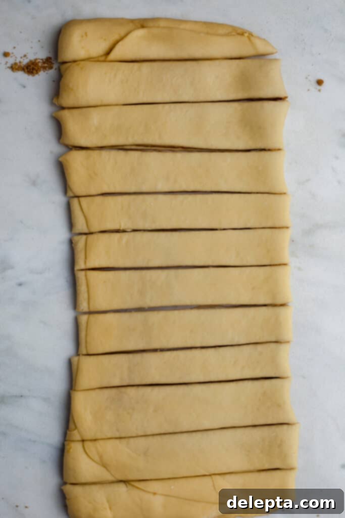 Pillowy Swedish Cinnamon Swirls 15 Neatly sliced strips of cinnamon bun dough, each approximately two centimeters wide, laid out on a clean surface, ready for twisting into individual buns.