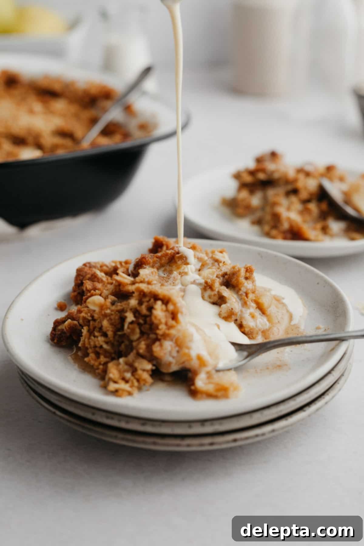 Warm Apple Crumble with Custard 2 A stack of small grey plates, the top one has apple crumble on it and there is custard being poured on it