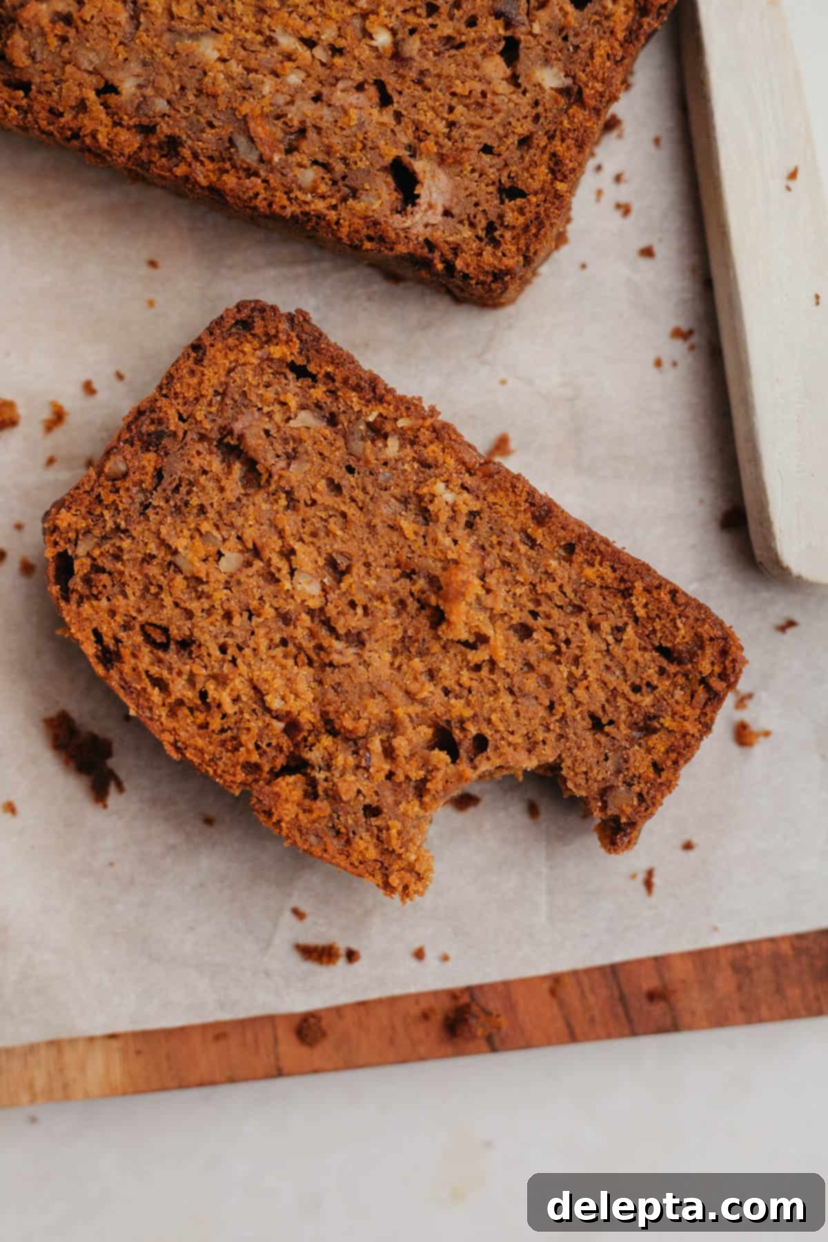 Effortless Pumpkin Carrot Banana Bread 7 A perfectly baked slice of healthy pumpkin banana bread resting on parchment paper, ready to be enjoyed.