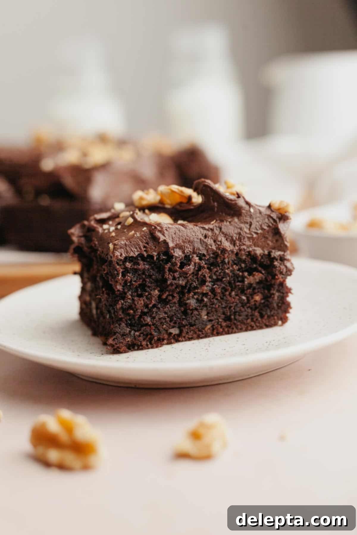 Simply Divine Moist Chocolate Walnut Cake 2 A perfectly sliced piece of moist chocolate walnut cake, topped with rich chocolate frosting and chopped walnuts, resting on a white plate.