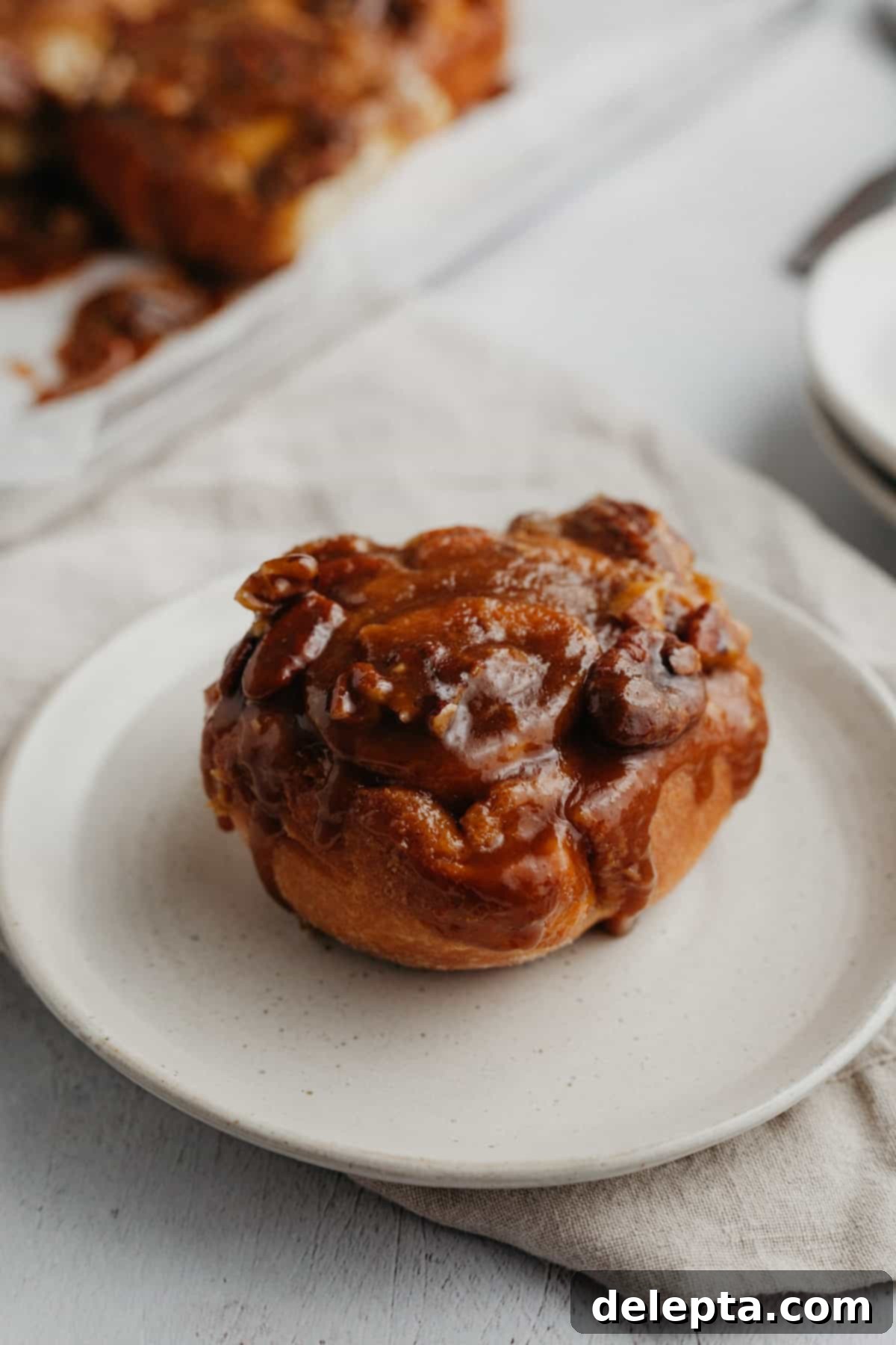 Decadent Pecan Caramel Rolls 2 A perfectly golden caramel cinnamon roll on a small beige plate, showcasing its gooey caramel top and soft interior.