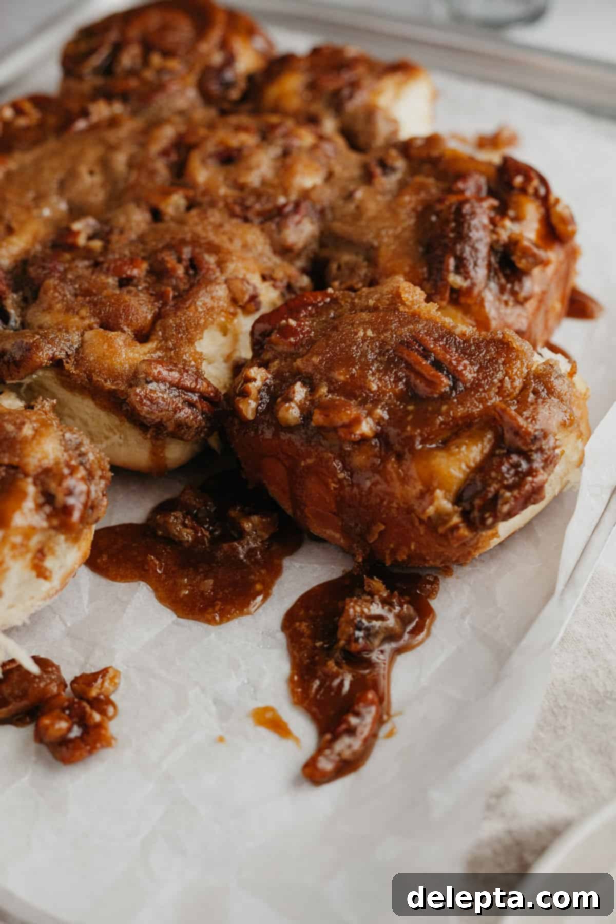 Decadent Pecan Caramel Rolls 10 Several freshly baked caramel cinnamon rolls cooling on parchment paper, their sticky, glistening tops visible.