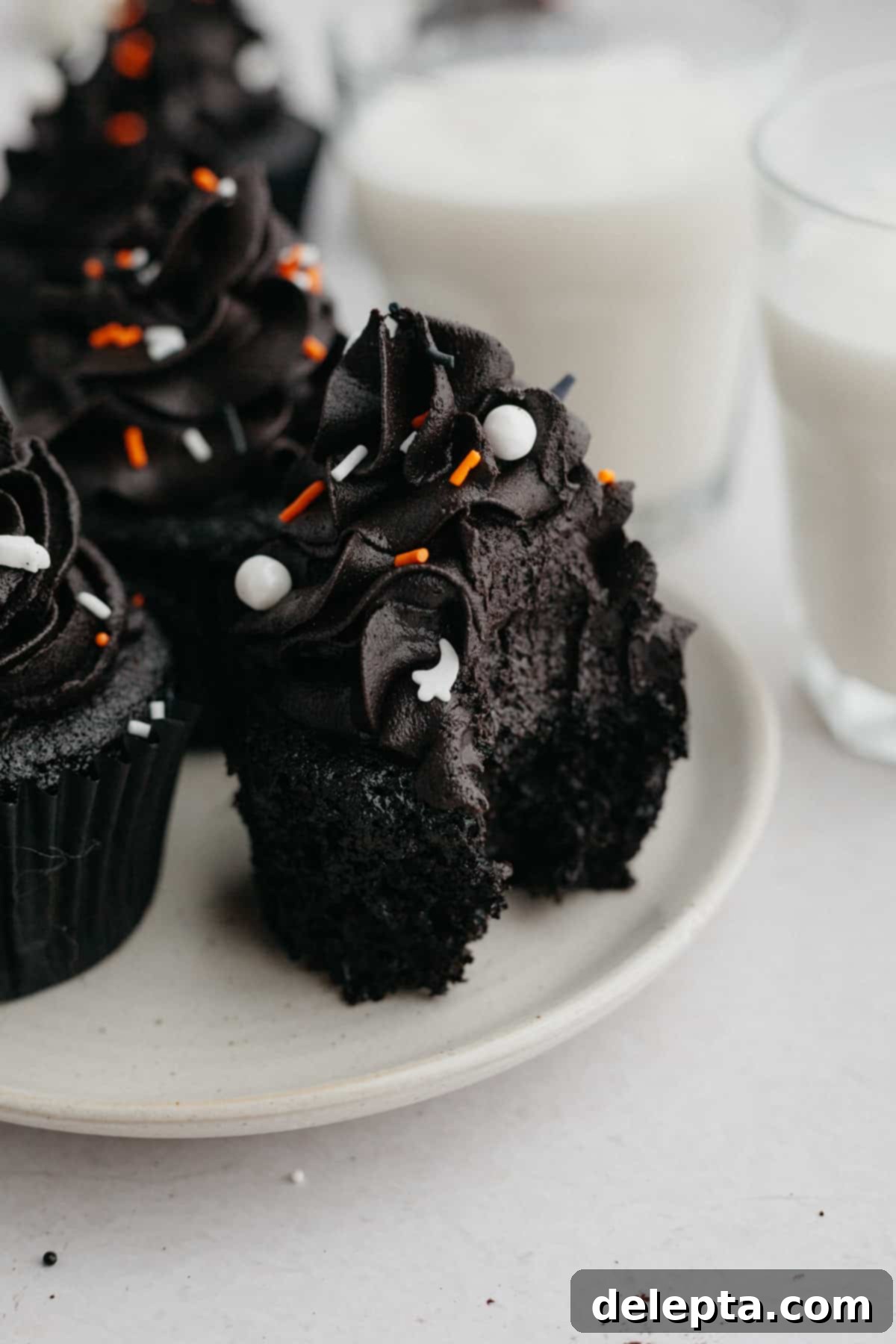 Midnight Velvet Delights 2 A perfectly baked and frosted black velvet cupcake with a bite taken out of it, revealing its dark interior.