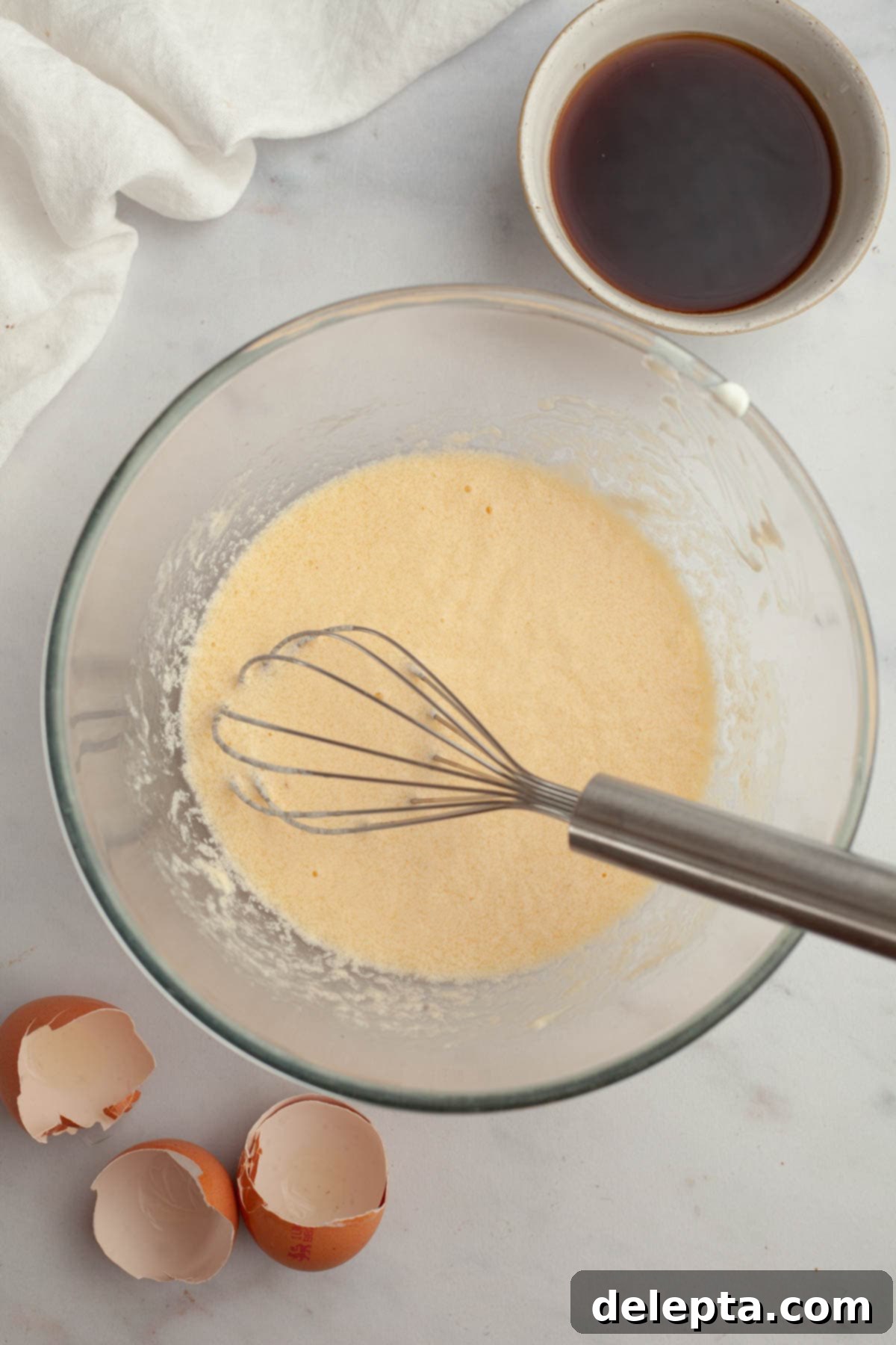 Quick Nutella-Stuffed Cupcakes 5 A glass bowl with a whisk and a beige liquid in it.
