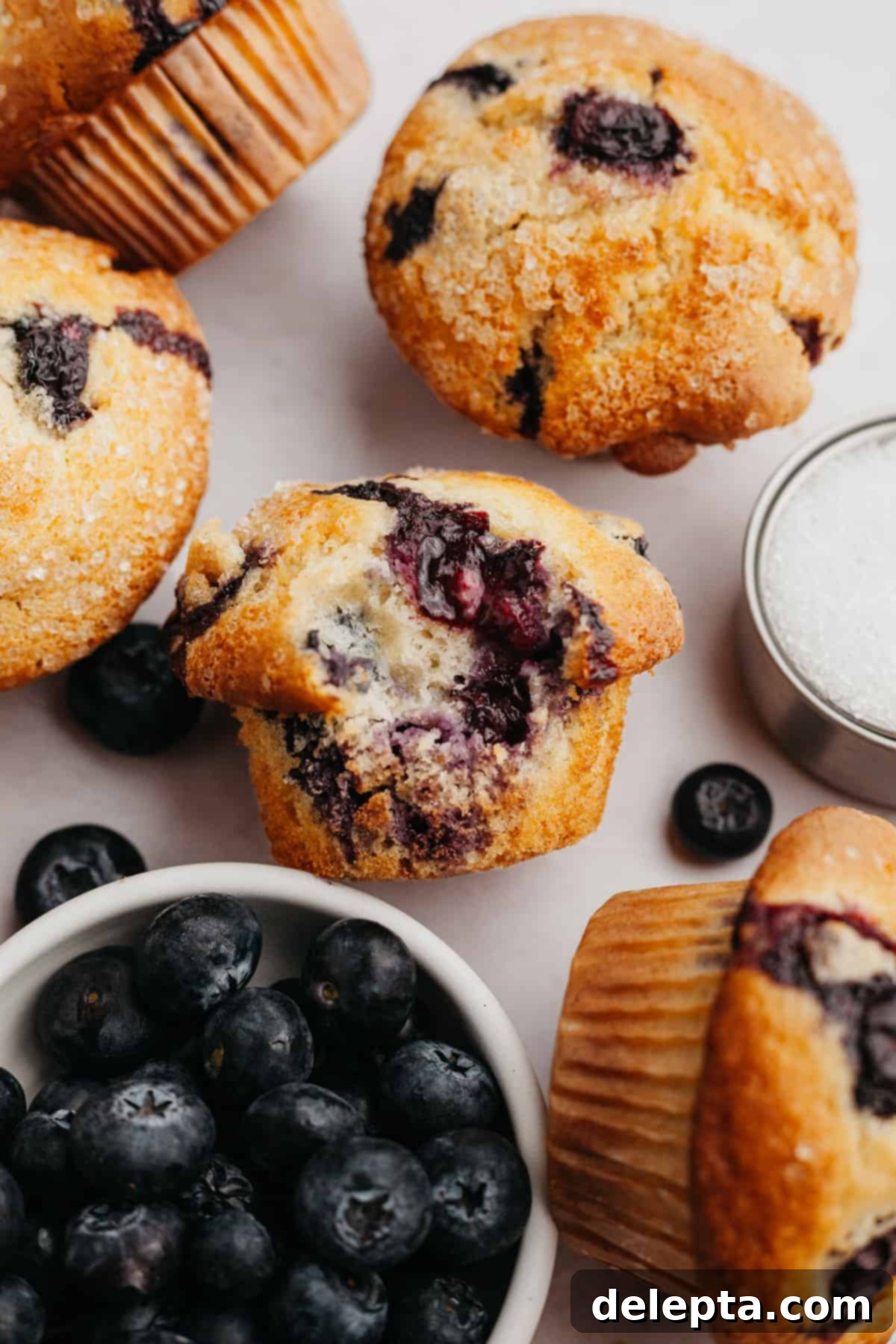 Signature Buttermilk Blueberry Muffins 2 A close up of a blueberry muffin with a bite taken out of it, showcasing its fluffy interior and juicy blueberries.