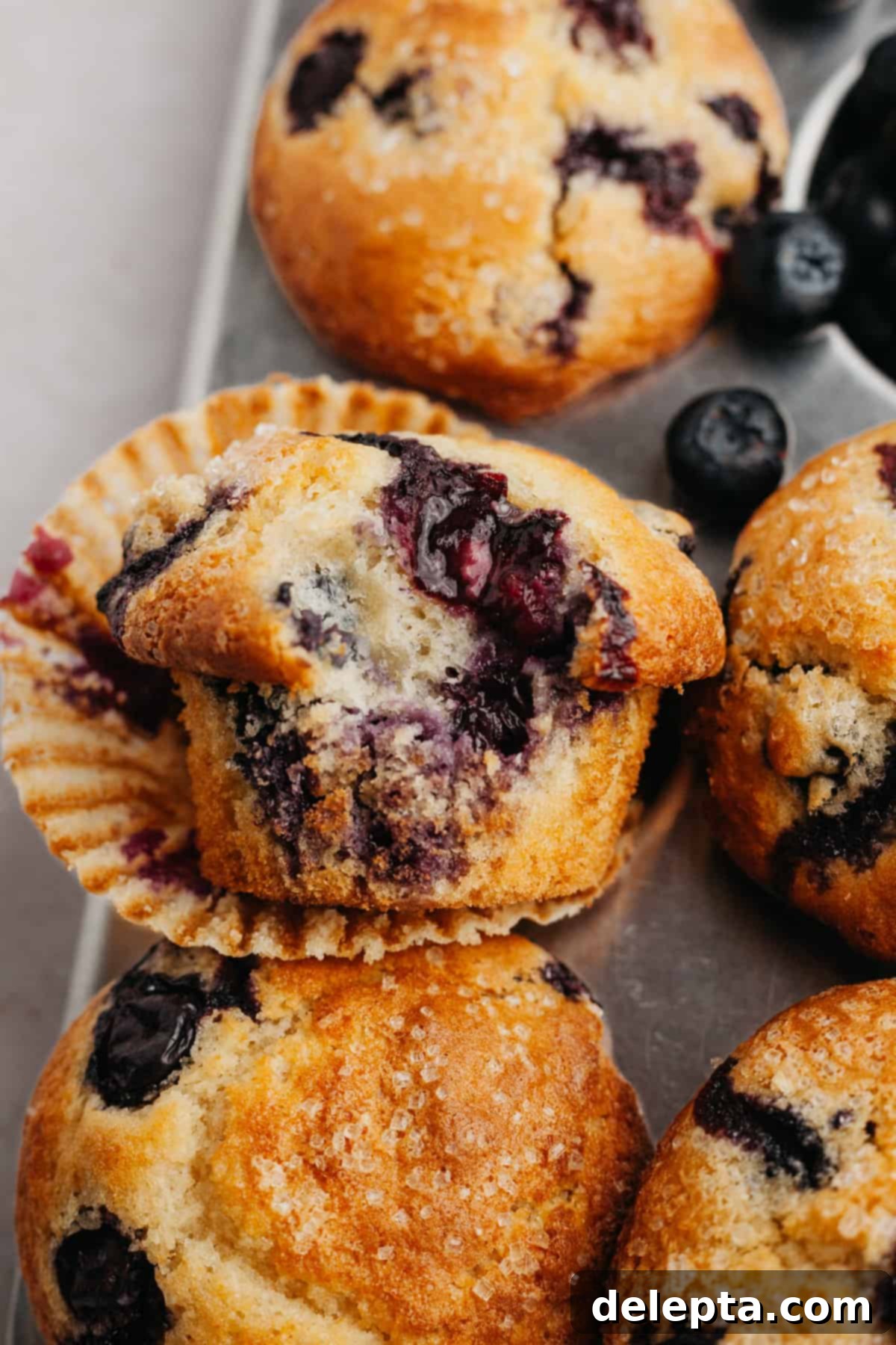 Signature Buttermilk Blueberry Muffins 7 A close up of a blueberry muffin with a bite taken out of it, showing its perfectly baked texture and juicy blueberries.