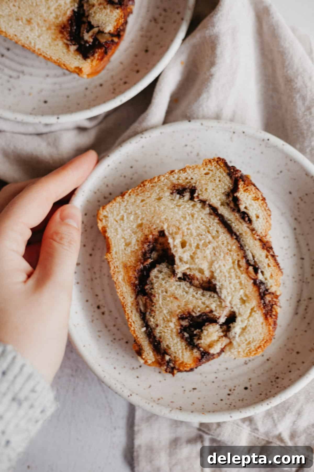 Decadent Nutella Babka 9 A speckled ceramic plate holds a perfectly cut slice of Nutella babka, revealing its intricate chocolate hazelnut swirls.