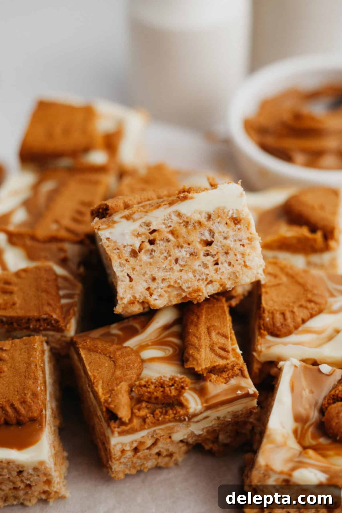 Ultimate Biscoff Krispie Bars 2 A pile of biscoff rice krispie treats, showcasing their gooey texture and white chocolate swirl with cookie pieces.