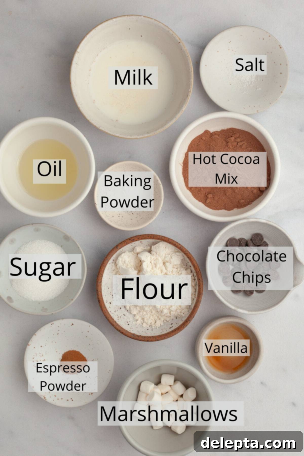 Mugful of Cocoa Bliss 3 All of the ingredients needed to make a hot cocoa mug cake, weighed out into small bowls, including flour, cocoa mix, oil, milk, and marshmallows.