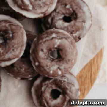 Decadent Glazed Chocolate Cake Doughnuts 9 A pile of chocolate cake doughnuts on parchment paper.