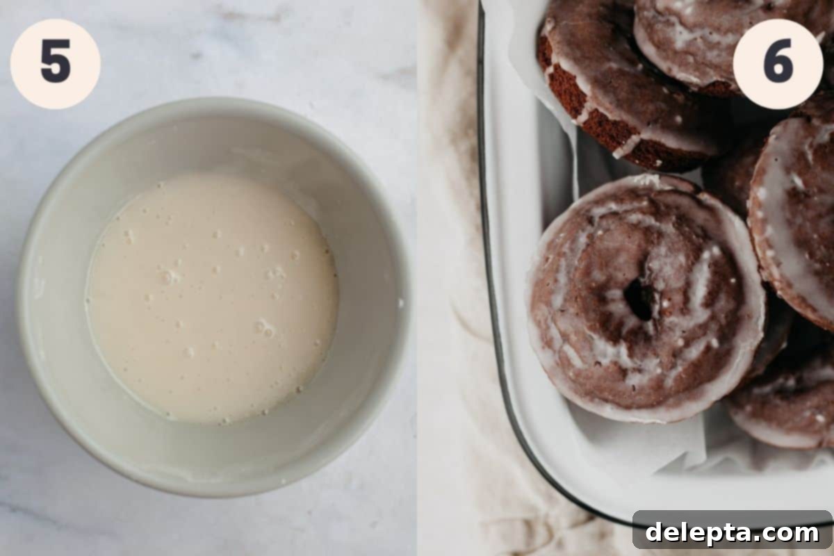 Decadent Glazed Chocolate Cake Doughnuts 6 A bowl filled with smooth vanilla glaze, positioned next to an enamel tray heaped with a pile of freshly baked chocolate donuts, depicting the glazing process.