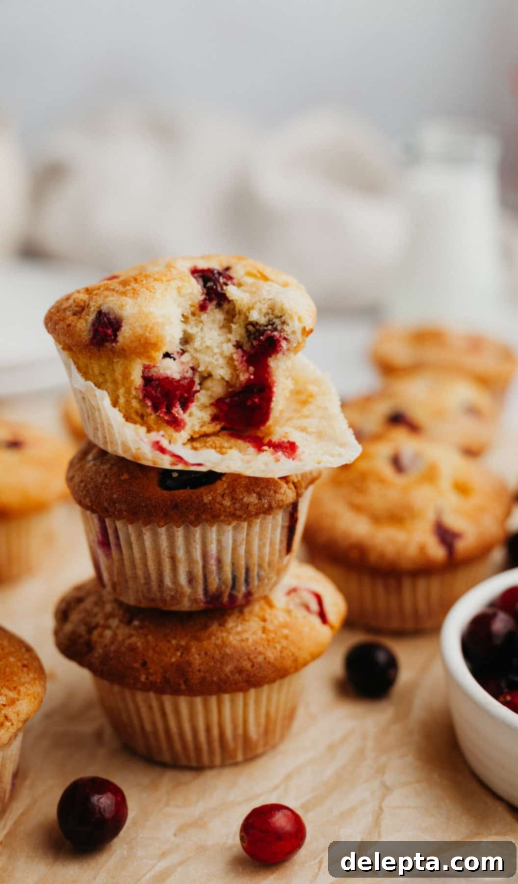 Bakery Fresh Cranberry White Chocolate Muffins 2 A stack of golden-brown cranberry white chocolate muffins, sprinkled with sparkling sugar, arranged artfully on parchment paper, ready to be enjoyed.
