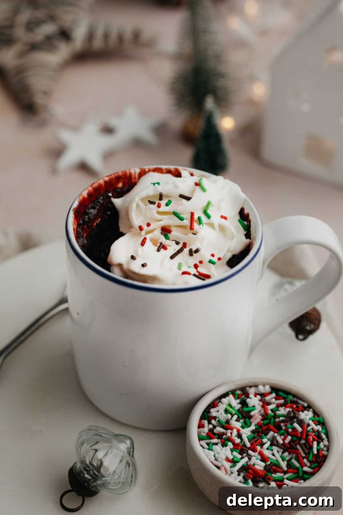 Velvet Mug Bliss 2 A red velvet mug cake topped with whipped cream and red and green sprinkles, ready to be enjoyed.