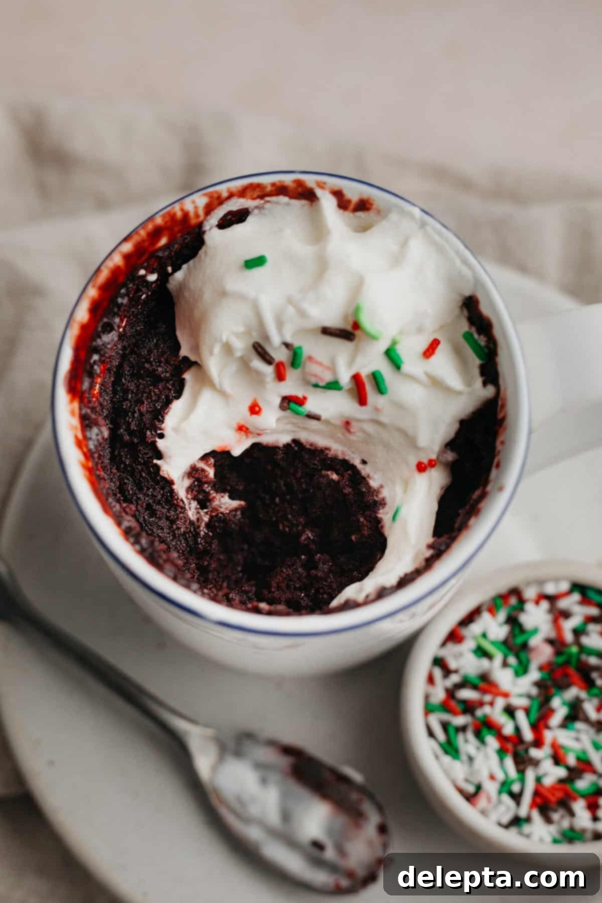 Velvet Mug Bliss 6 A vibrant red velvet mug cake, perfectly baked and topped with luscious whipped cream and festive red and green sprinkles.
