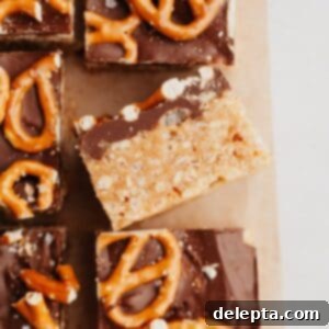 Decadent Chocolate Peanut Butter Rice Krispie Treats 9 Pretzel topped chocolate peanut butter rice krispie treats on parchment paper, one is on it's side.