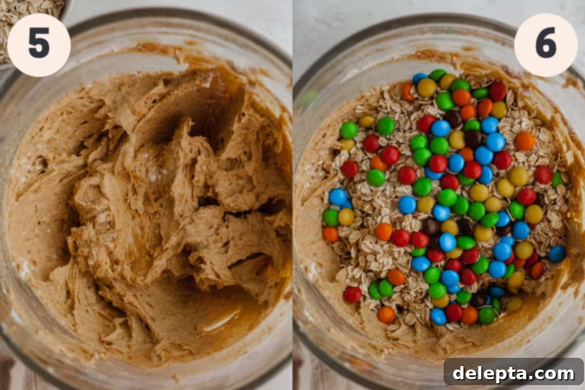 M and M Loaded Peanut Butter Oatmeal Cookies 6 A glass mixing bowl filled with oatmeal peanut butter cookie dough, topped with rolled oats and colorful M&Ms, ready to be folded in.