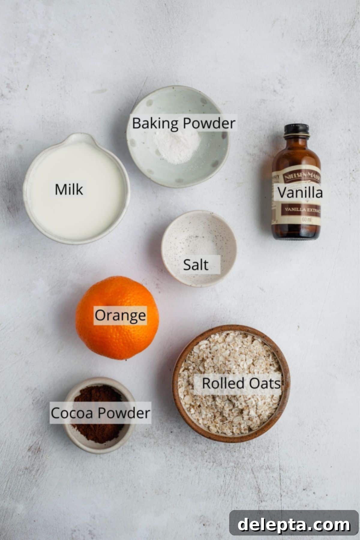 Sunshine Chocolate Orange Baked Oats 3 All the ingredients for chocolate orange baked oats neatly laid out in small bowls, including oats, cocoa powder, orange slices, and milk.