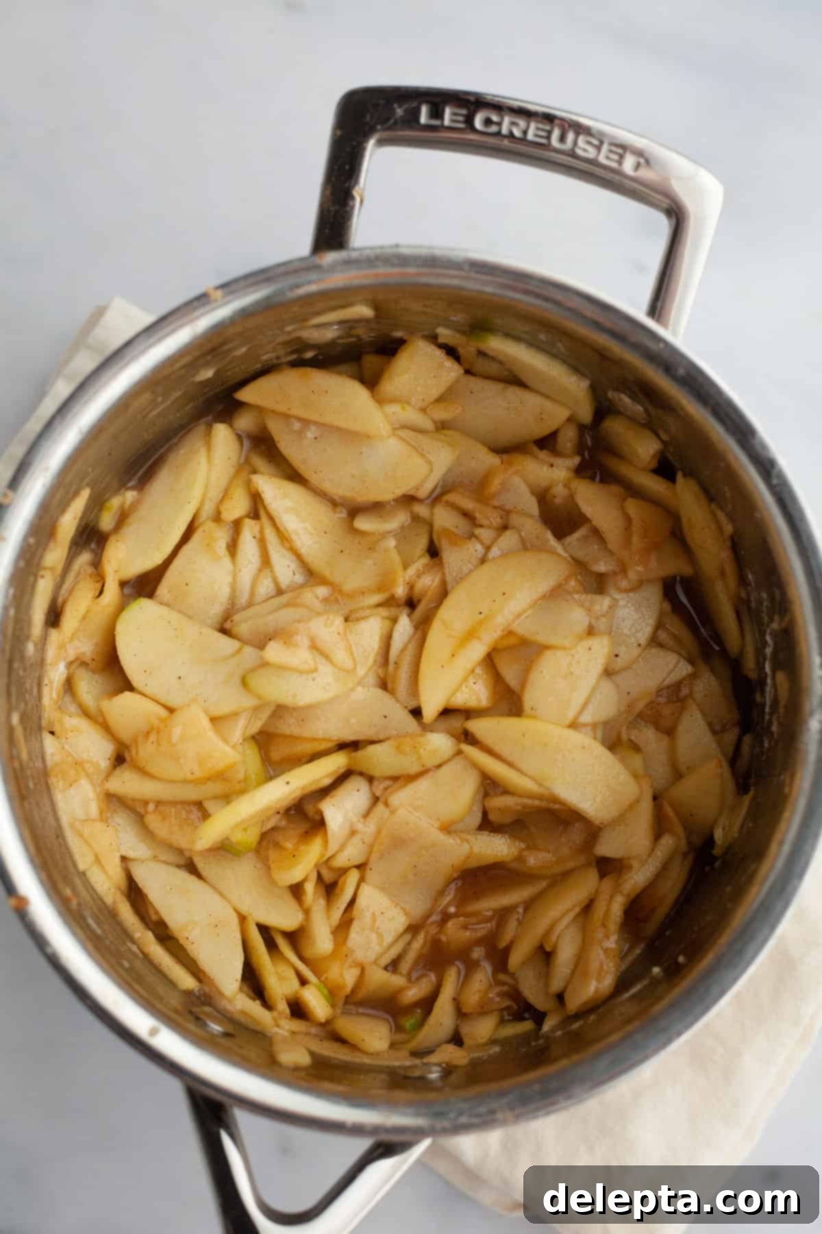 Fireside Bourbon Apple Pie 11 A silver saucepan with a bubbling apple pie filling, rich with spices and syrup, cooking on the stovetop.