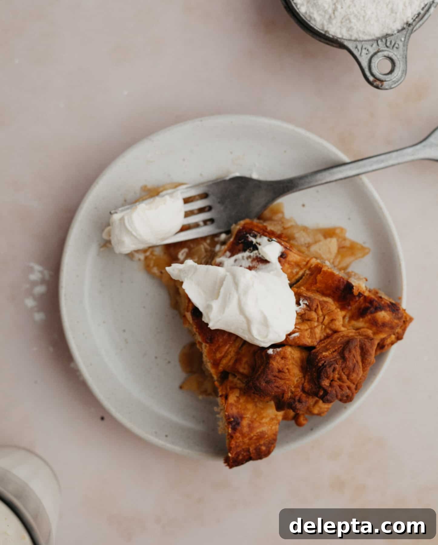 Fireside Bourbon Apple Pie 15 A delectable slice of bourbon apple pie on a small white plate, adorned with a generous dollop of homemade whipped cream, ready to be enjoyed.
