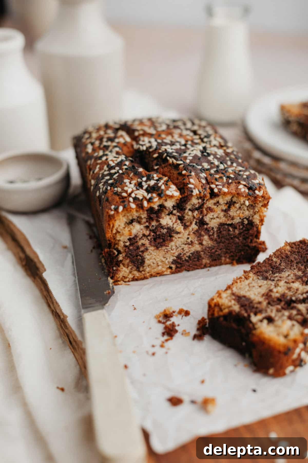 Chocolate-Tahini Swirled Banana Bread with Creamy Tang 2 A beautifully swirled chocolate tahini banana bread loaf on parchment paper, with one slice perfectly cut and displayed.