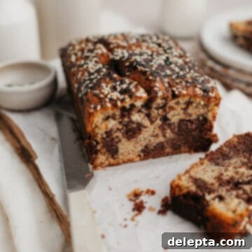 Chocolate-Tahini Swirled Banana Bread with Creamy Tang 10 a swirled tahini banana bread on parchment paper, one slice has been cut off.