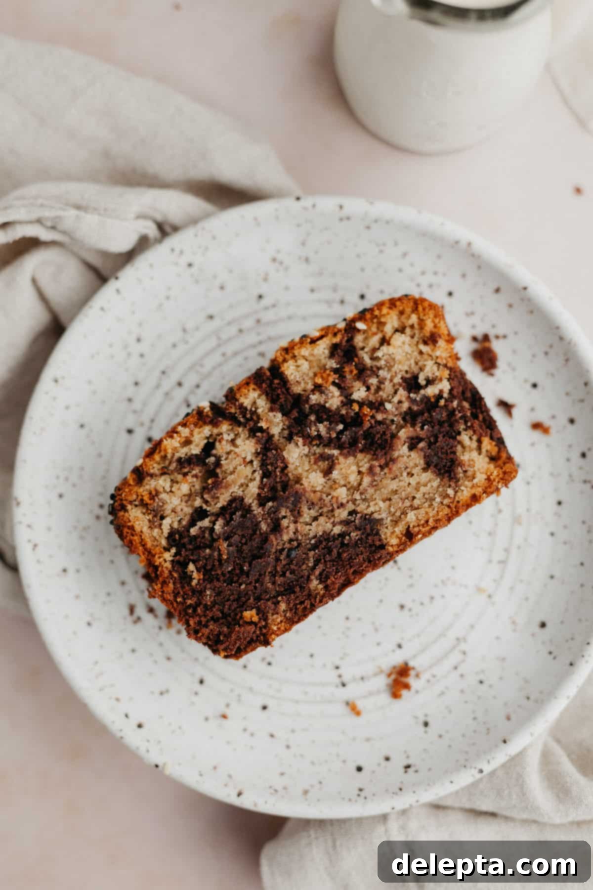Chocolate-Tahini Swirled Banana Bread with Creamy Tang 9 A perfectly baked slice of swirled chocolate tahini banana bread displayed on a small white plate, showcasing its intricate pattern.