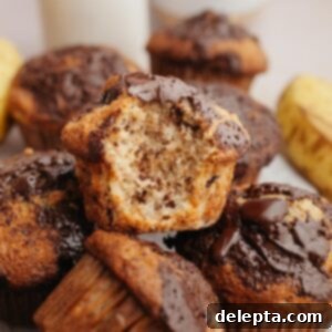Gourmet Chocolate Chunk Banana Muffins 10 A delicious pile of freshly baked chocolate chunk banana muffins, with one muffin having a bite taken out, revealing its moist interior.