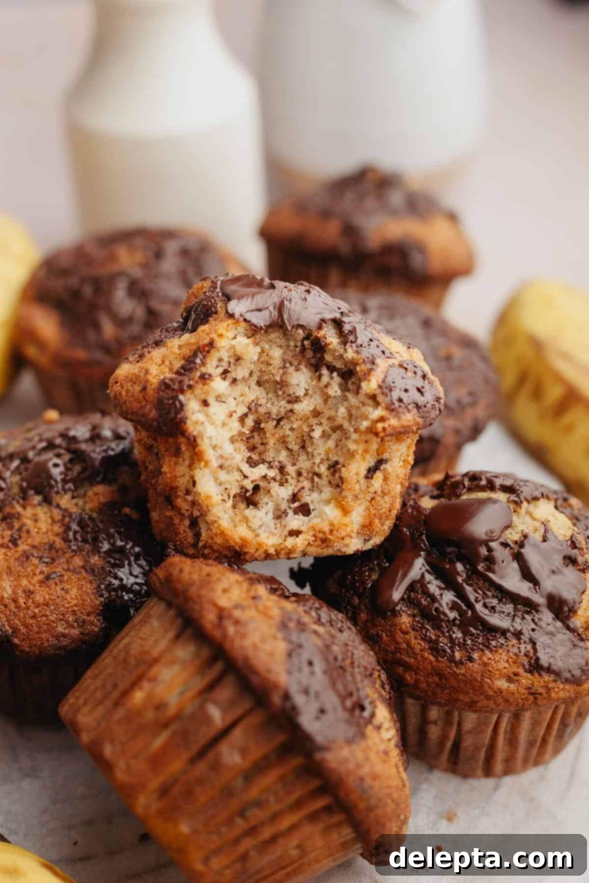 Gourmet Chocolate Chunk Banana Muffins 9 A delectable pile of banana muffins, one with a delightful bite taken out of it, showcasing the moist interior and melted chocolate chunks.