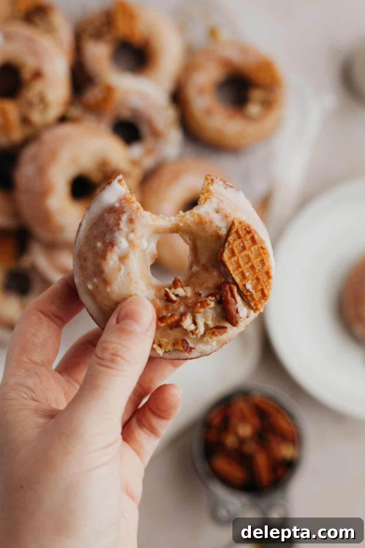 Irresistible Baked Maple Doughnuts 7 A white hand gently holding a freshly glazed maple donut, which has a small bite taken out, showcasing its fluffy texture.
