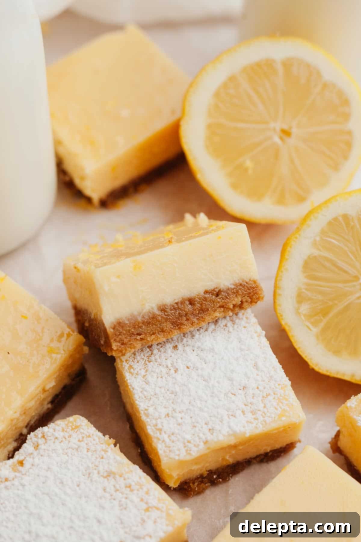Zesty Lemon Squares with Buttery Graham Crust 2 Freshly baked lemon squares on parchment paper, some delicately dusted with powdered sugar, ready to be enjoyed.