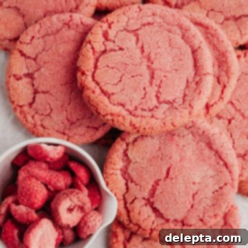 Perfectly Pink, Soft-Chewy Sugar Cookies 9 several pink sugar cookies on parchment paper with a small bowl of freeze dried strawberries.