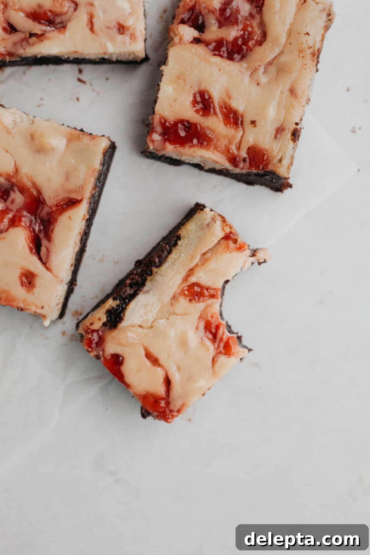 Irresistible Strawberry Cheesecake Brownies from Scratch 11 Several strawberry swirled cheesecake brownies on parchment paper.