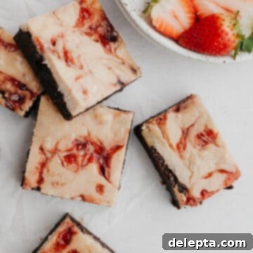 Irresistible Strawberry Cheesecake Brownies from Scratch 12 Several strawberry cheesecake brownies on parchment paper with several sliced strawberries on a grey plate.