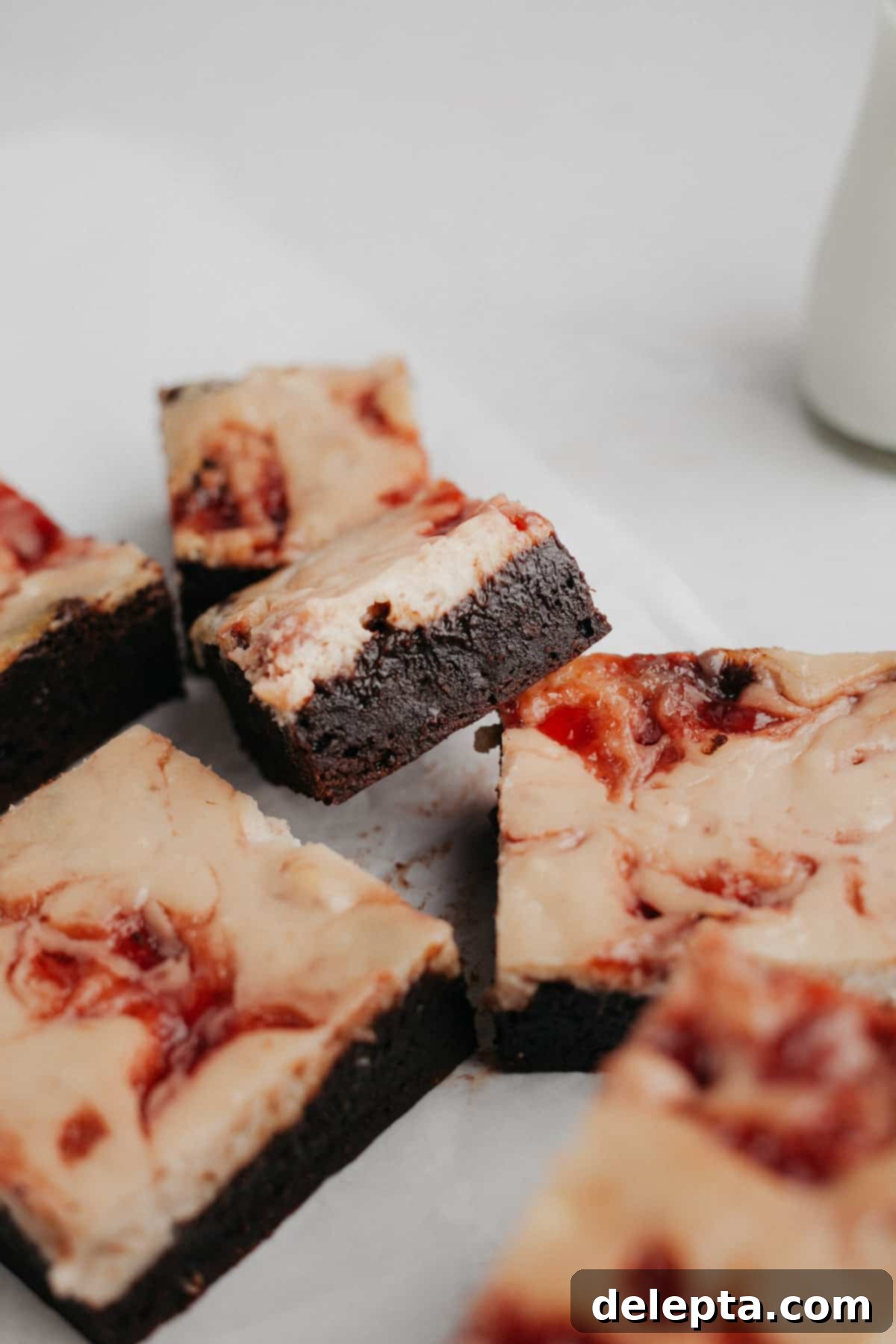 Irresistible Strawberry Cheesecake Brownies from Scratch 10 Several strawberry swirled cheesecake brownies on parchment paper.
