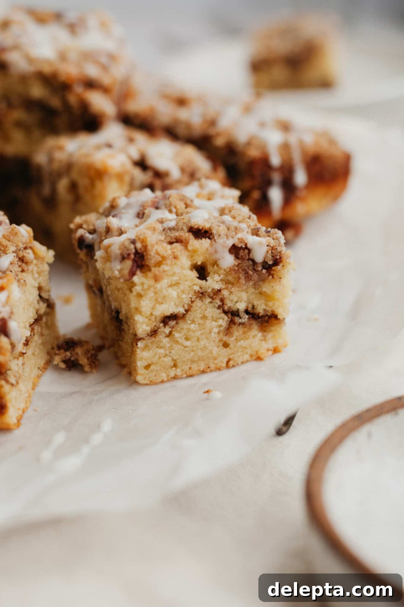 Heavenly Pecan Sour Cream Coffee Cake 2 A close up of a slice of pecan sour cream coffee cake on parchment paper, showcasing its moist texture and rich layers.
