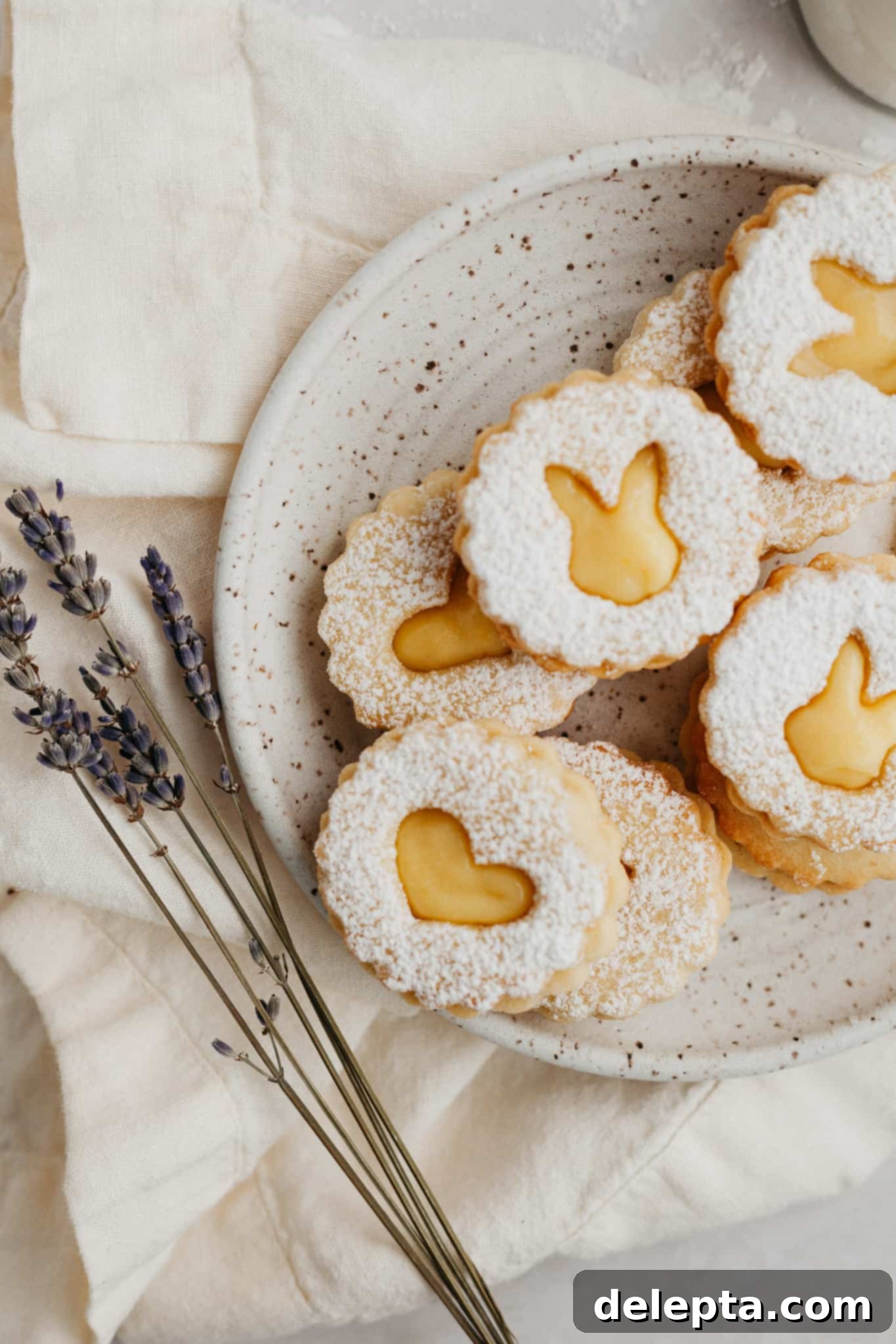 Zesty Lemon Curd Delights 10 A small speckled beige plate presenting a stack of heart-shaped lemon curd cookies, beautifully dusted with confectioners' sugar, highlighting their delicious filling.