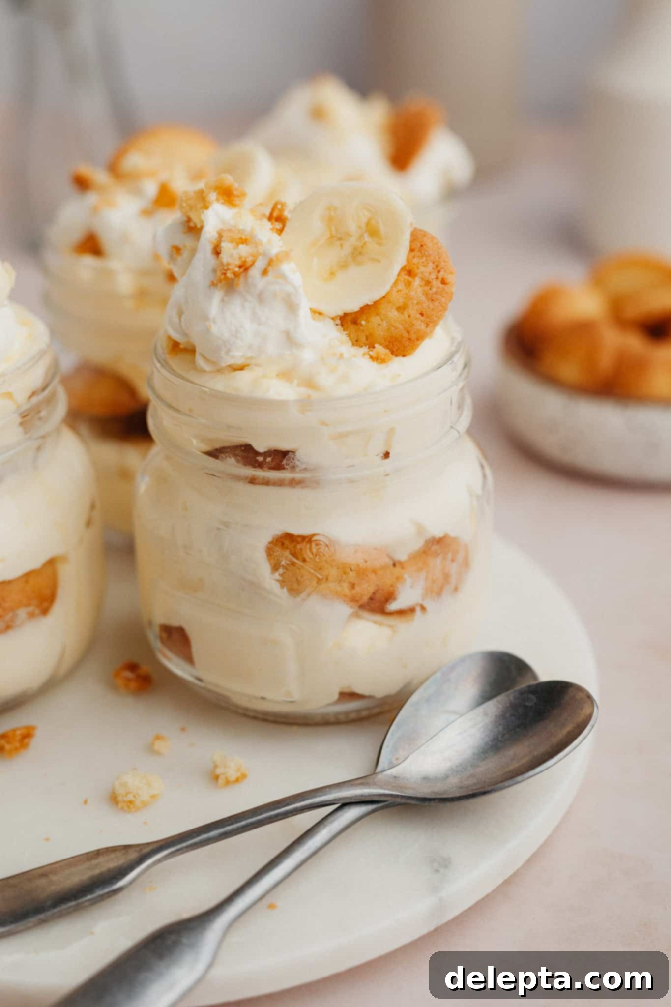 Jarred Banana Pudding Bliss 2 A close up of individual banana pudding in a jar on a marble surface, ready to be enjoyed.