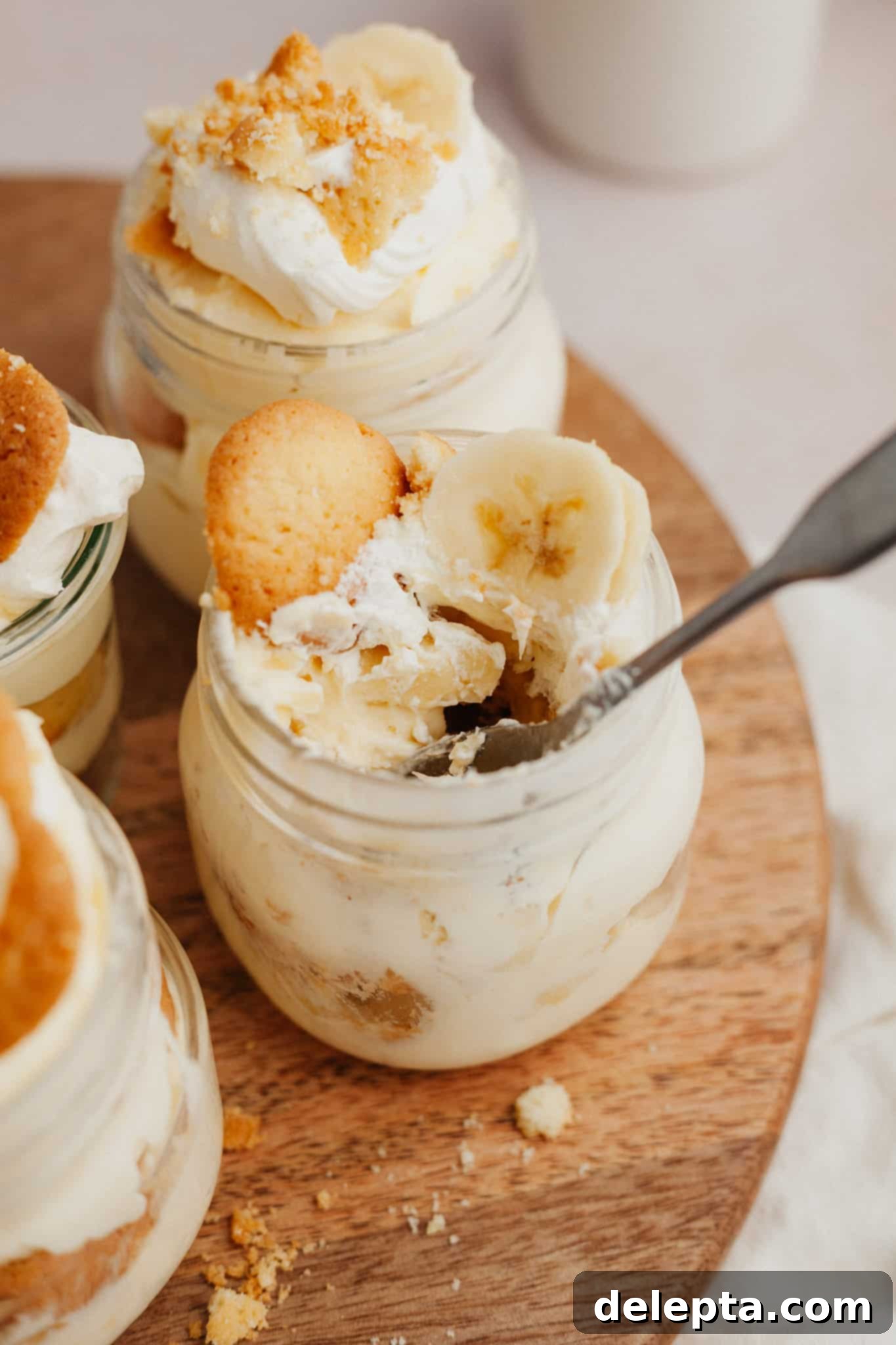 Jarred Banana Pudding Bliss 8 Beautifully layered banana pudding in a jar on a wooden board, with a spoon in the jar ready to scoop.