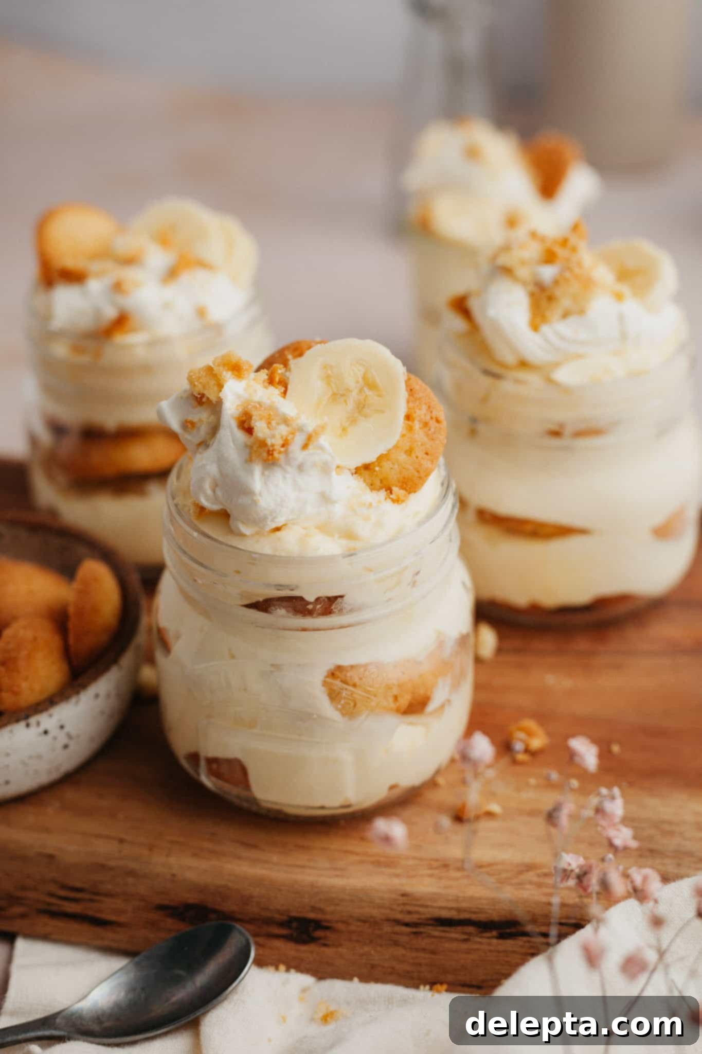 Jarred Banana Pudding Bliss 9 Four jars of banana pudding arranged neatly on a rustic wooden board, showcasing their layers.