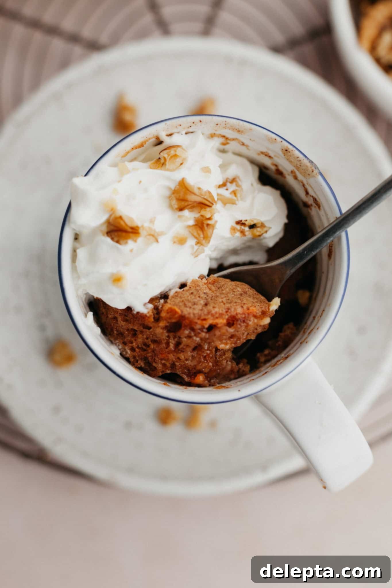 Warm Spiced Carrot Mug Delight 2 An inviting overhead shot of a moist carrot mug cake generously topped with fluffy whipped cream and a sprinkle of chopped nuts.